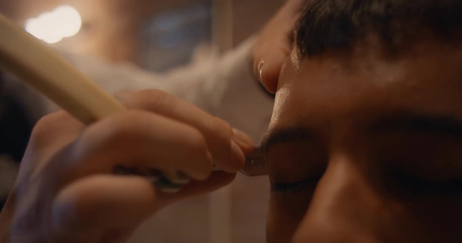 A barber trims a teenagers sideburn with a blade