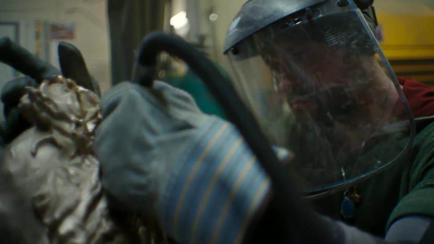 A metal sculptor using a drill to sculpt a metallic head