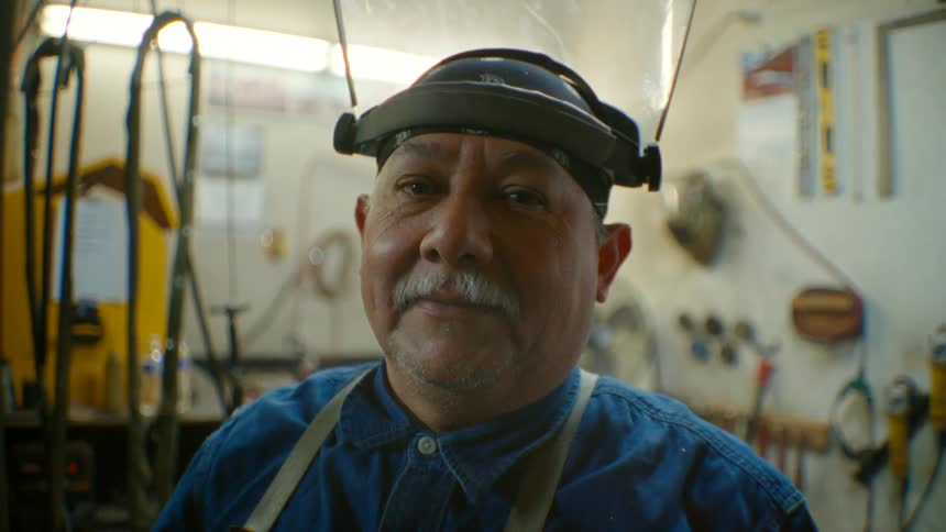A man stands in his workshop with a face guard flipped up