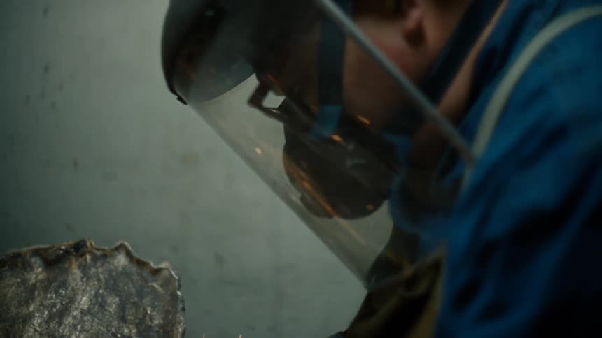 A welder wears a protective face mask while working with metal