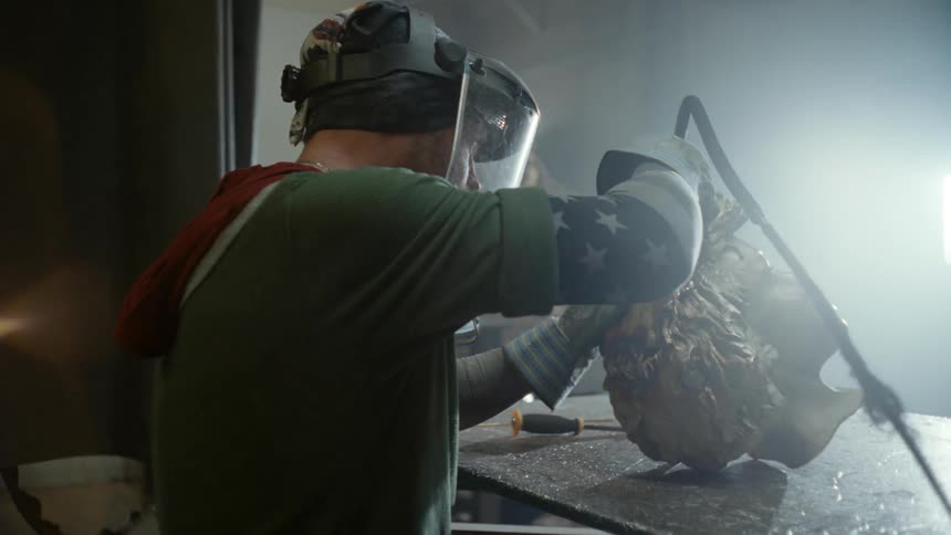 Sculptor working on a metal statue head over the workbench in a workshop