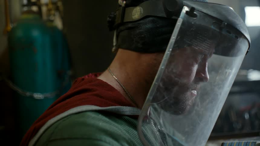 A man wearing a protective face shield works on a small sculpture