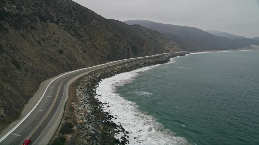Low flying aerial footage of cars approaching and following the coastal Highway 1 near Point Mugu California