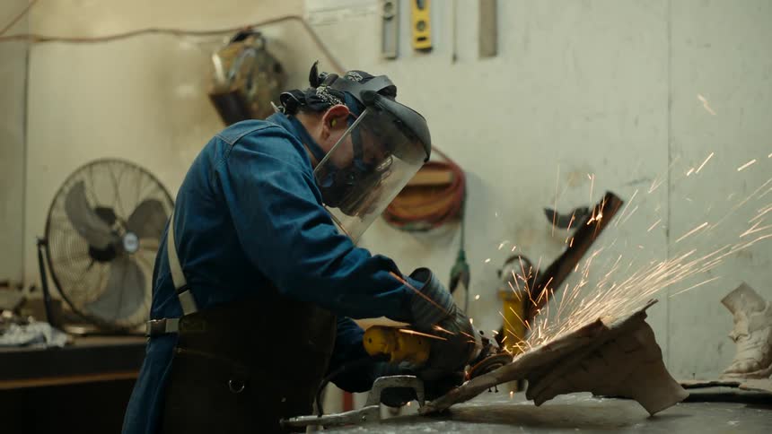 Close up of a sculptor cutting piece of metal over a workbench in his workshop