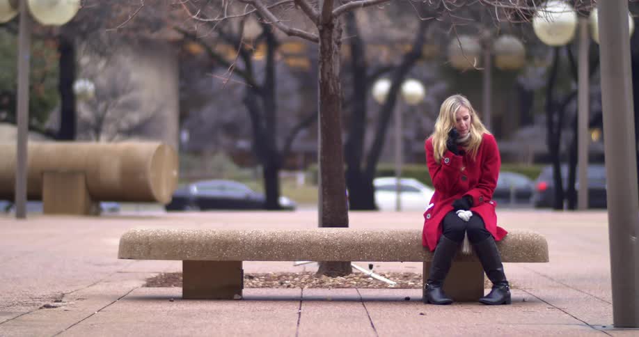 A woman sitting on a bench outside talking on her cell phone