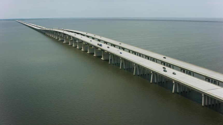 Traffic moves over the water on a long bridge with land in the far distance