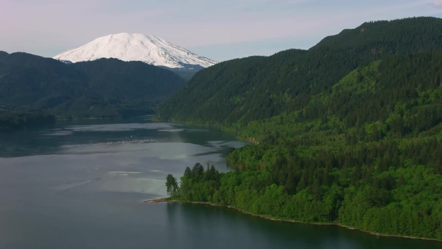 Aerial view moving over mountain valley lake surrounded by wilderness and snowcapped mountain in the background