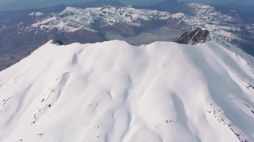 An aerial of a snow covered volcano with ridges along the peak also covered in snow