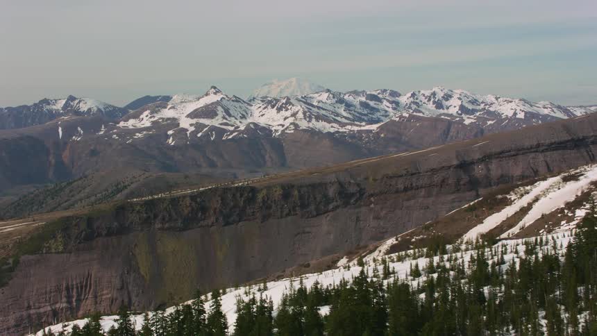 Aerial view of snowcovered mountain range with wilderness coniferous trees and mountain pass daytime
