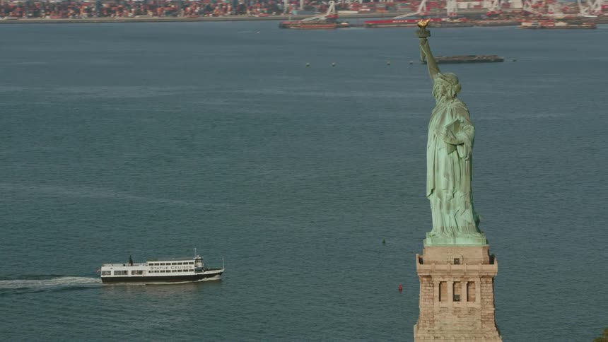 Ships move through water between waterfront and the statue of liberty
