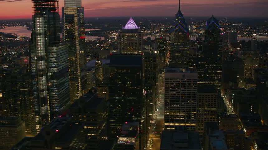 An aerial view of a riverfront city and its skyscrapers lit up at dusk