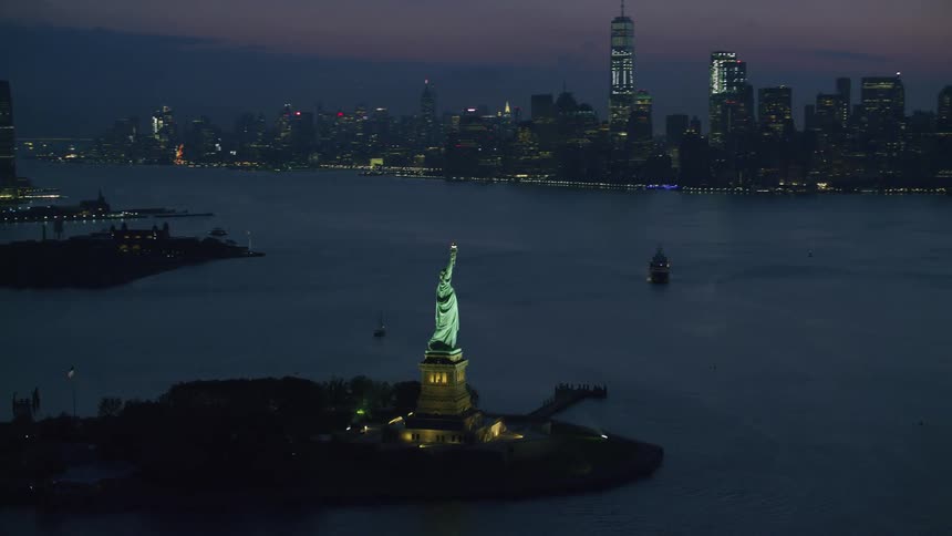 An aerial view of the statue of liberty at night with the city skyline in the distance