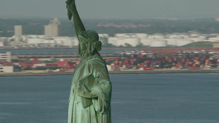 The statue of liberty stands tall overlooking new york harbor with holding her torch high in the air as boats sail in the water and city buildings are in the distance