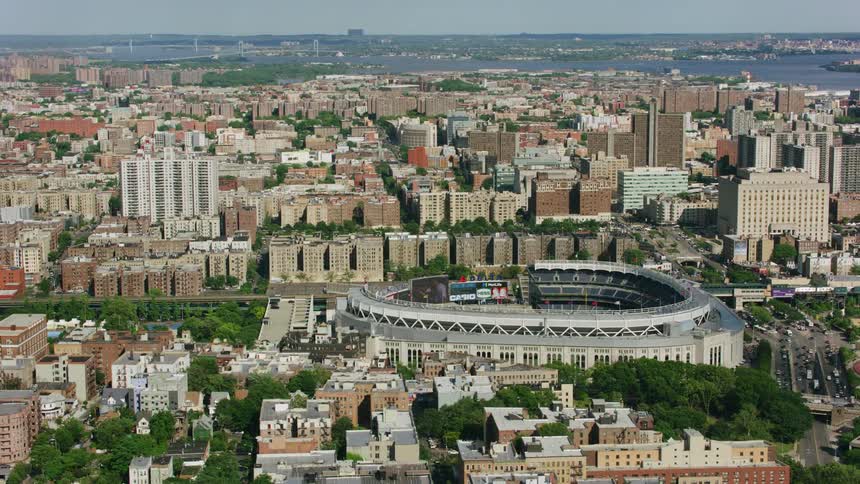 An aerial view of an arena in the middle of a dense urban city with the ocean in the distance