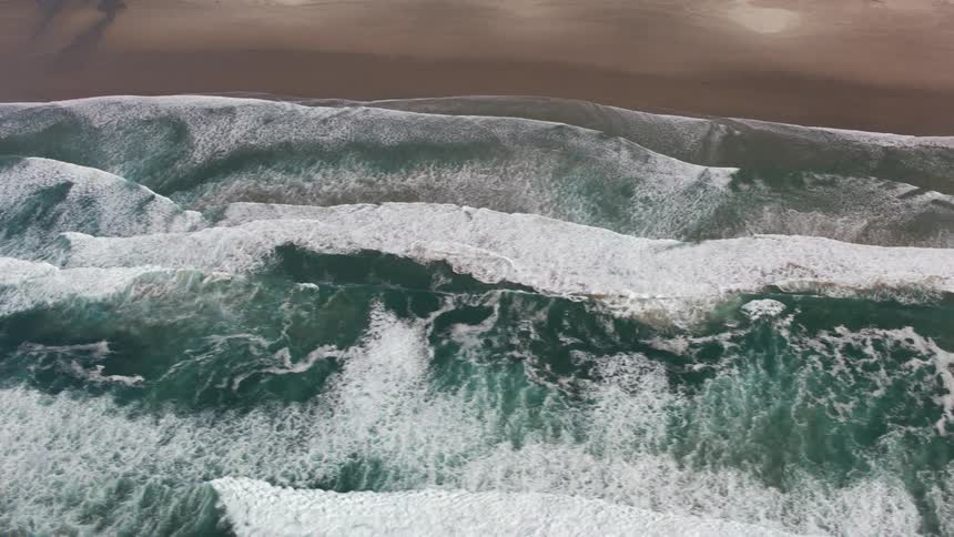 Aerial view moving along the shore of a florida beach with white sand and green water