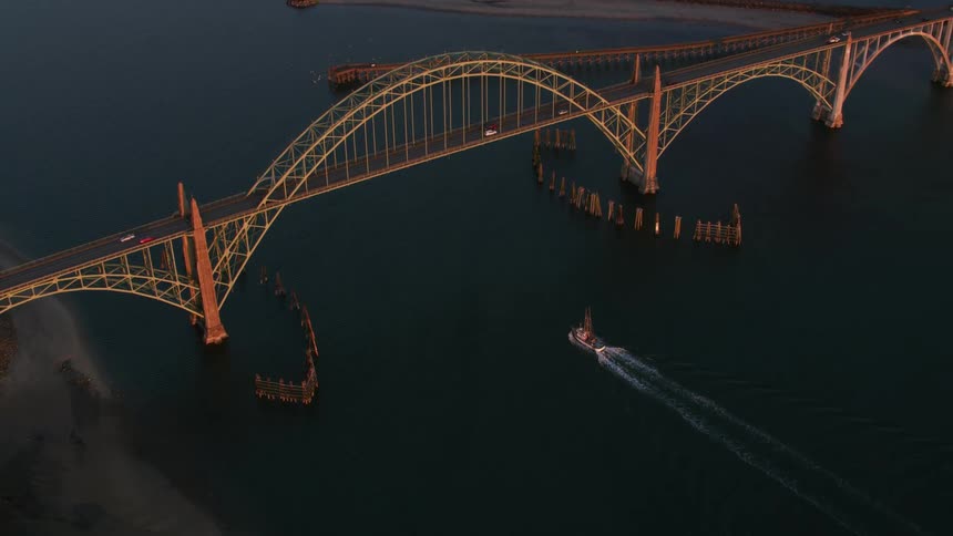 Aerial view of boats sailing under an arched bridge on a waterfront town