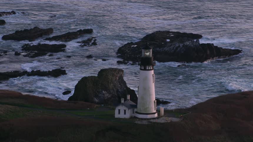 An aerial camera rotates around a lighthouse on a rocky coast near the sea