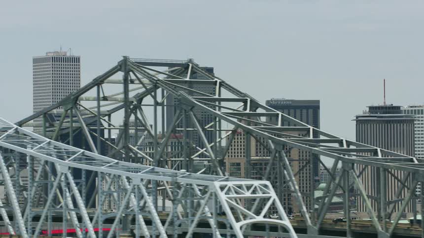 An aerial of a city skyline and an arch bridge close up with cars traveling on it