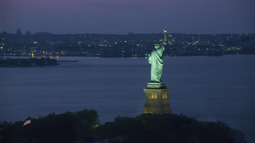 A statue situated near the ocean in a city that boasts large houses
