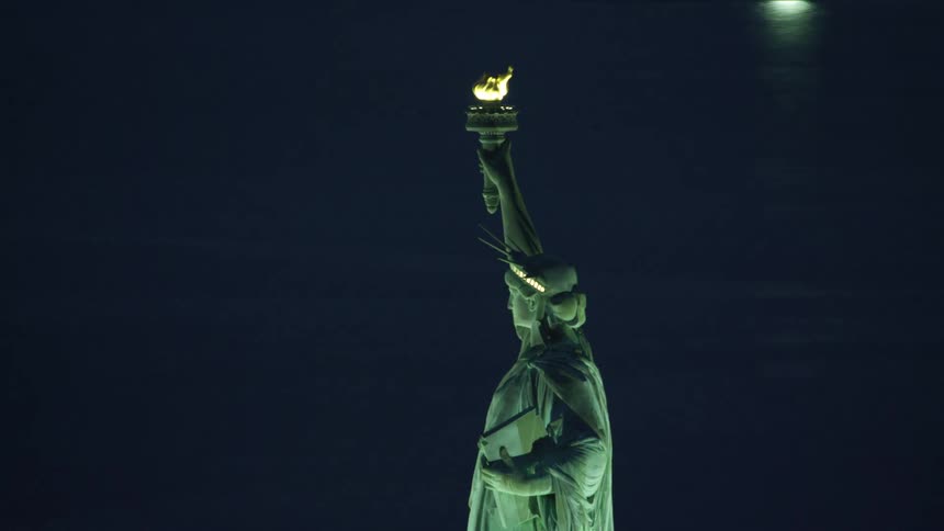 Ships sitting in the water around the statue of liberty shine light onto reflective water