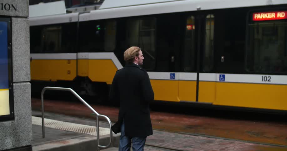 A man stopping to wait for a commuter train to pass before he continues to walk
