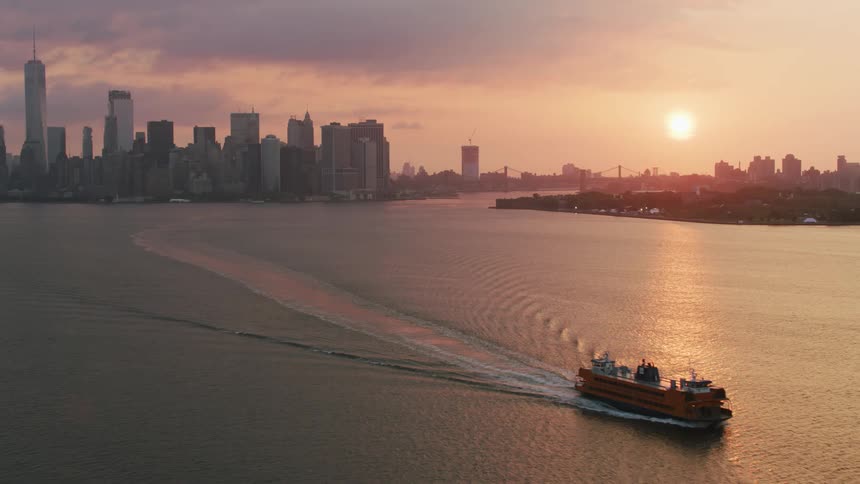 Sun sets over a ferry sailing on a river in next to new york city