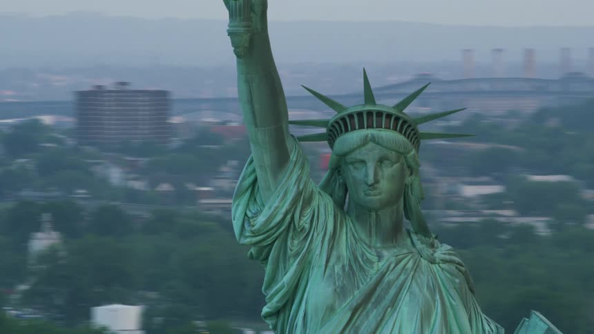 The statue of liberty stands tall overlooking the hudson river with the city in the distance