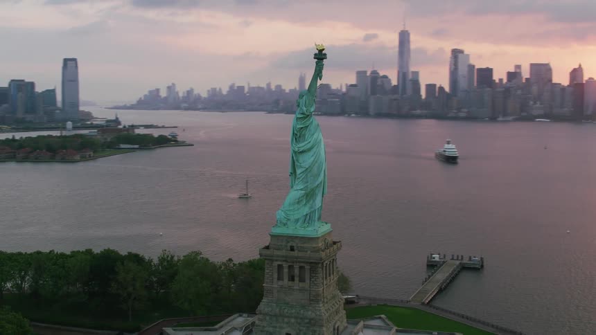 An aerial shot of the statue of liberty on an island at sunset