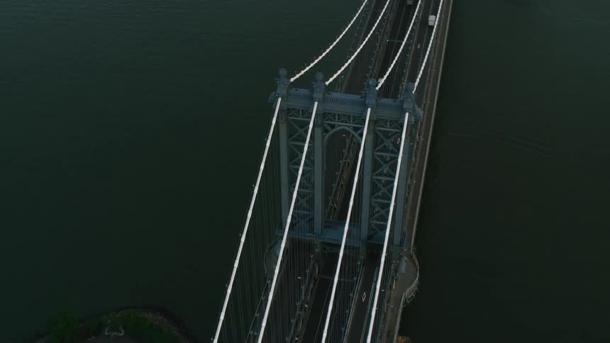 An aerial of an archway bridge over water with traffic traveling on it connecting to suburb land