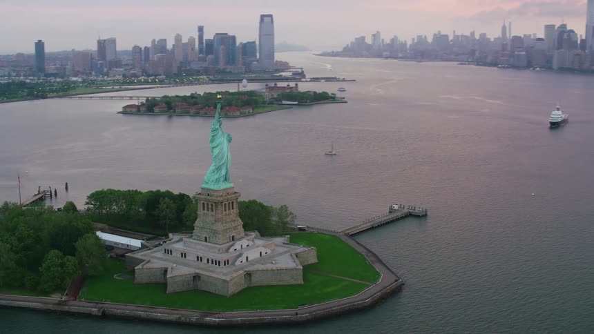 A dusk view of the statue of liberty and the city skyline behind it
