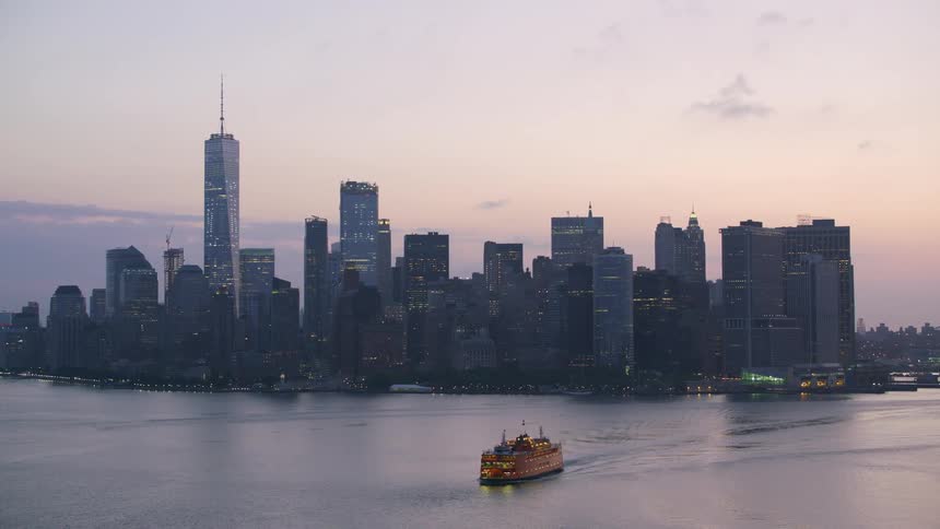 Aerial view of ship traveling on water near the city skyline at dusk