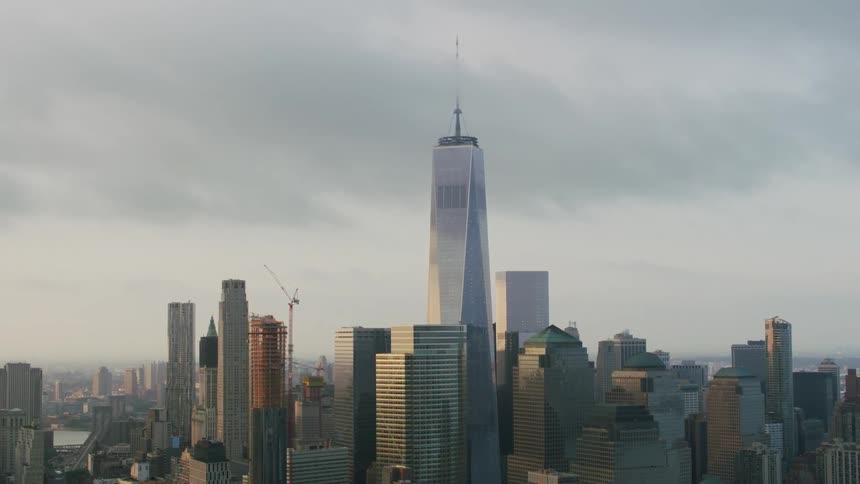 Skyscraper under construction stands among buildings surrounding one world trade center near the waterfront on an overcast day