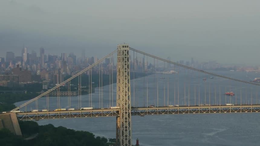 Aerial view of vehicles driving over a bridge next to new york city skyline