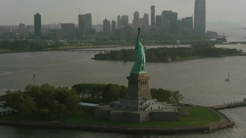 A statue standing tall close to a very big city during the dawn