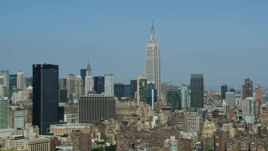 Bird flies over downtown as one dark skyscraper near the empire state building briefly reflects the sun