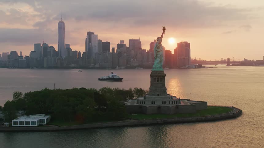 Aerial view of statue of liberty on liberty island and city skyline as the sun goes down