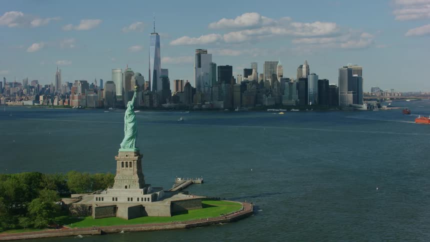 An aerial of the statue of liberty on an island with the city skyline in the background