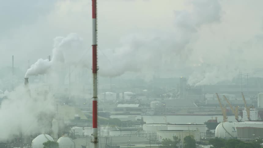 An industrial setting with the presence of smoke a tank a road and moving cars
