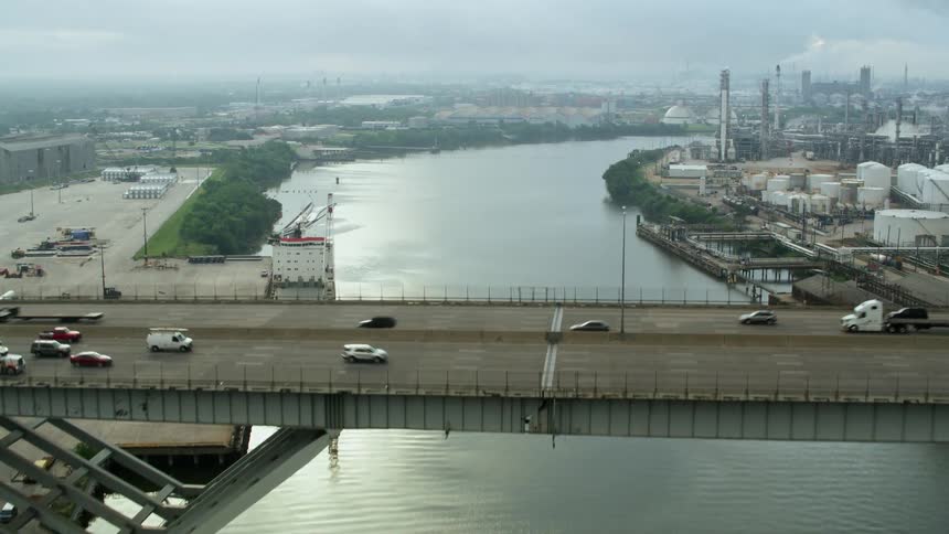 An aerial camera flies along a waterway over a bridge near urban factories