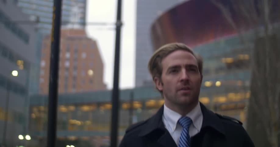 A man in a coat and tie walks down a city street