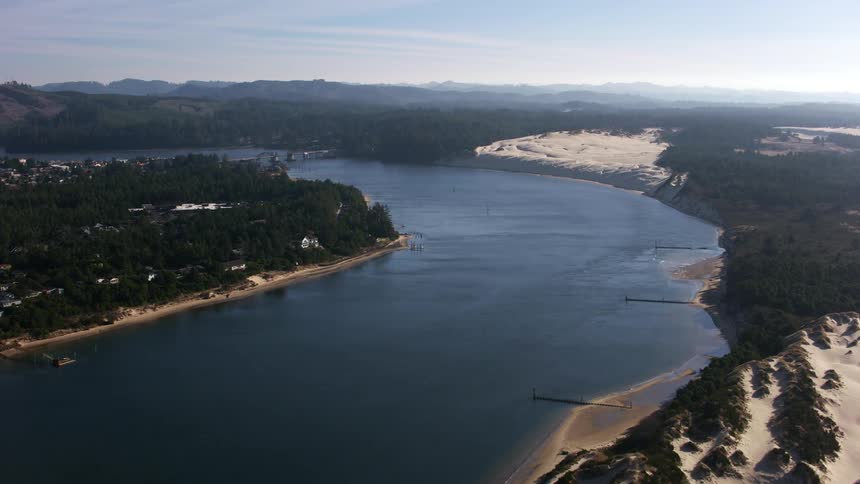 A body of water between land masses including an island with trees and a village and a sandy beach