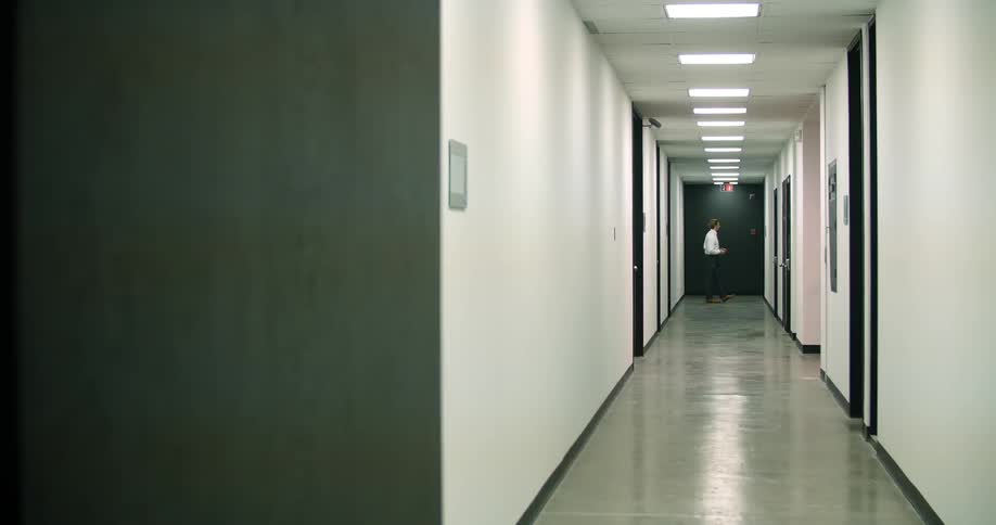 A man standing and turning at the end of a long hallway
