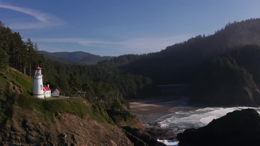 People stand near lighthouse on forested mountain and look out to sea