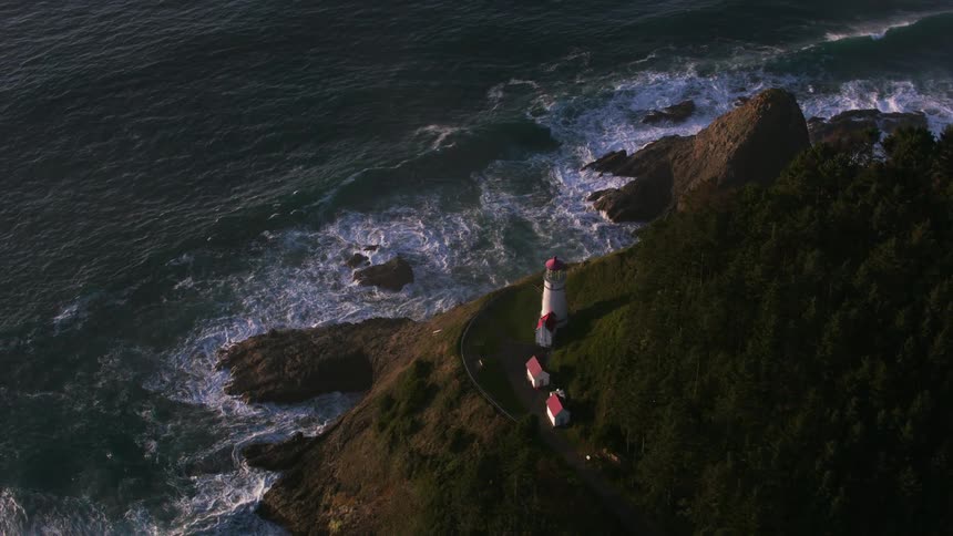 Aerial view of a lighthouse over a promontory next to the ocean at evening