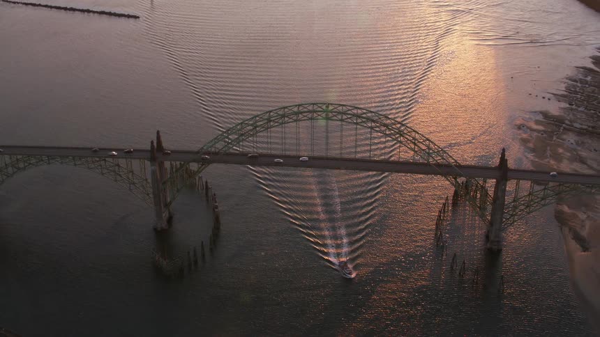 An aerial view of an active bridge with a boat moving through the water underneath it at sunset
