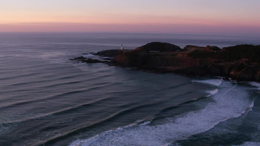 An aerial shot of a lighthouse on the shoreline at dusk