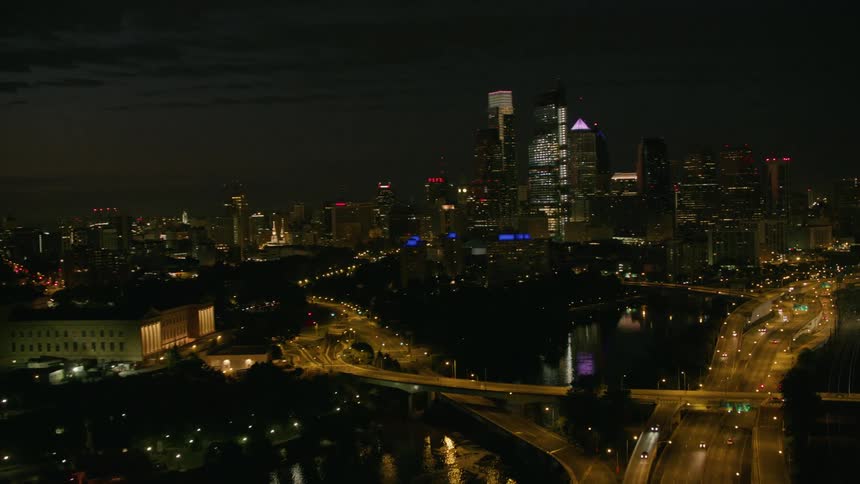 Traffic drives along highway over reflective water near downtown at night