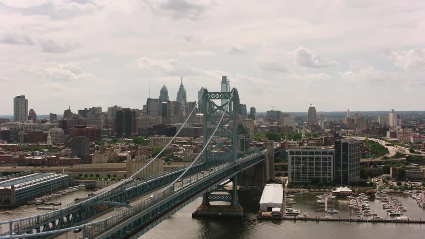 An aerial of an archway bridge going over a river on the outskirts of a metropolis city with tall buildings