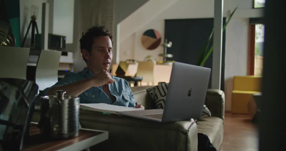 Man with blue shirt and writes down while making video call in the living room at home