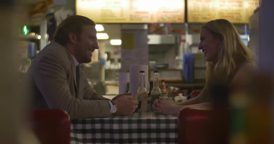 Man and woman sit at a table in a diner talking